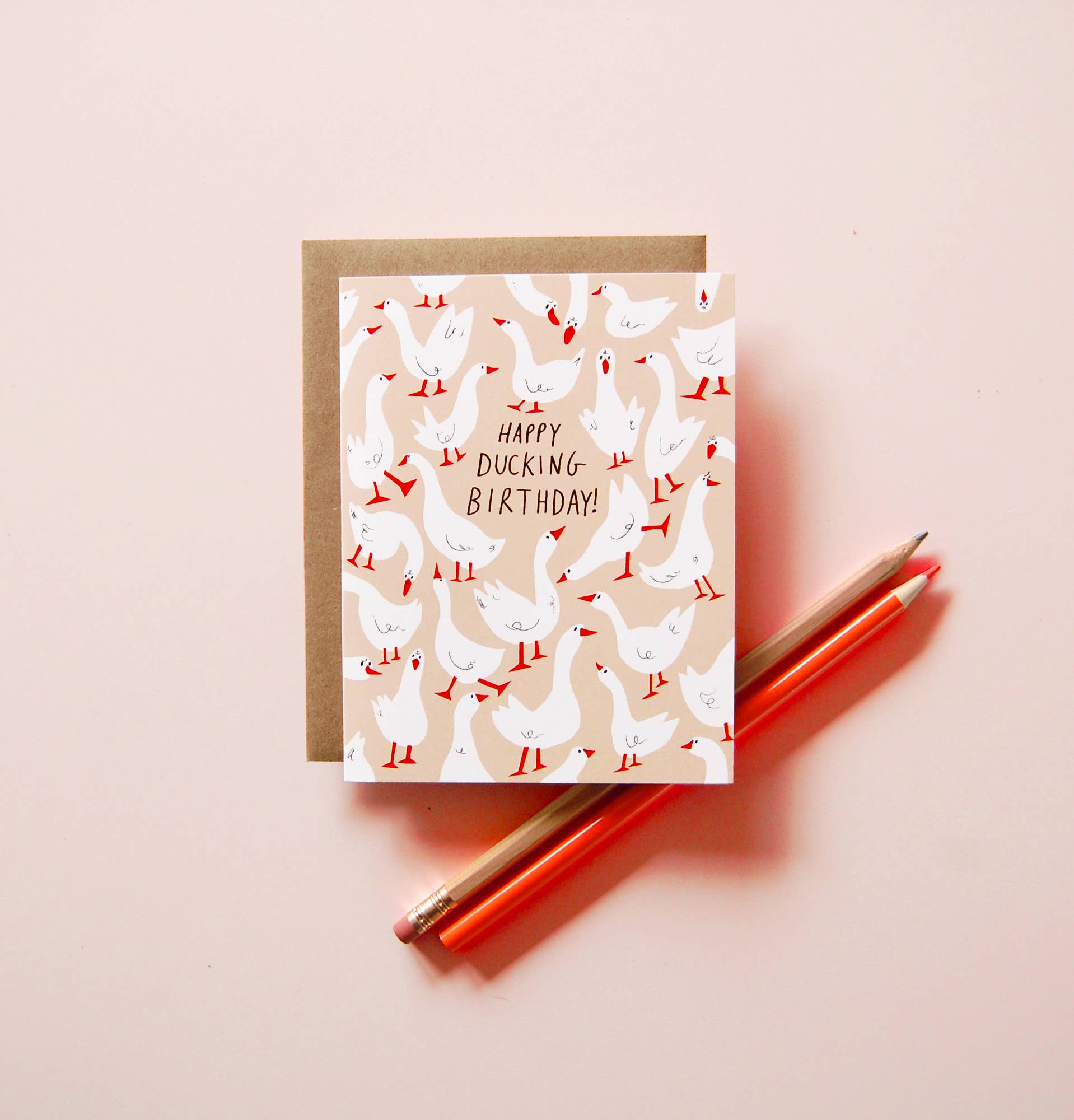 Happy Ducking Birthday Card by Badger & Burke featuring illustrated white ducks on a peach background with a kraft envelope.
