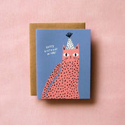 Spotted Cat Birthday Card by Badger & Burke featuring a pink spotted cat wearing a black-and-white party hat on a blue background.