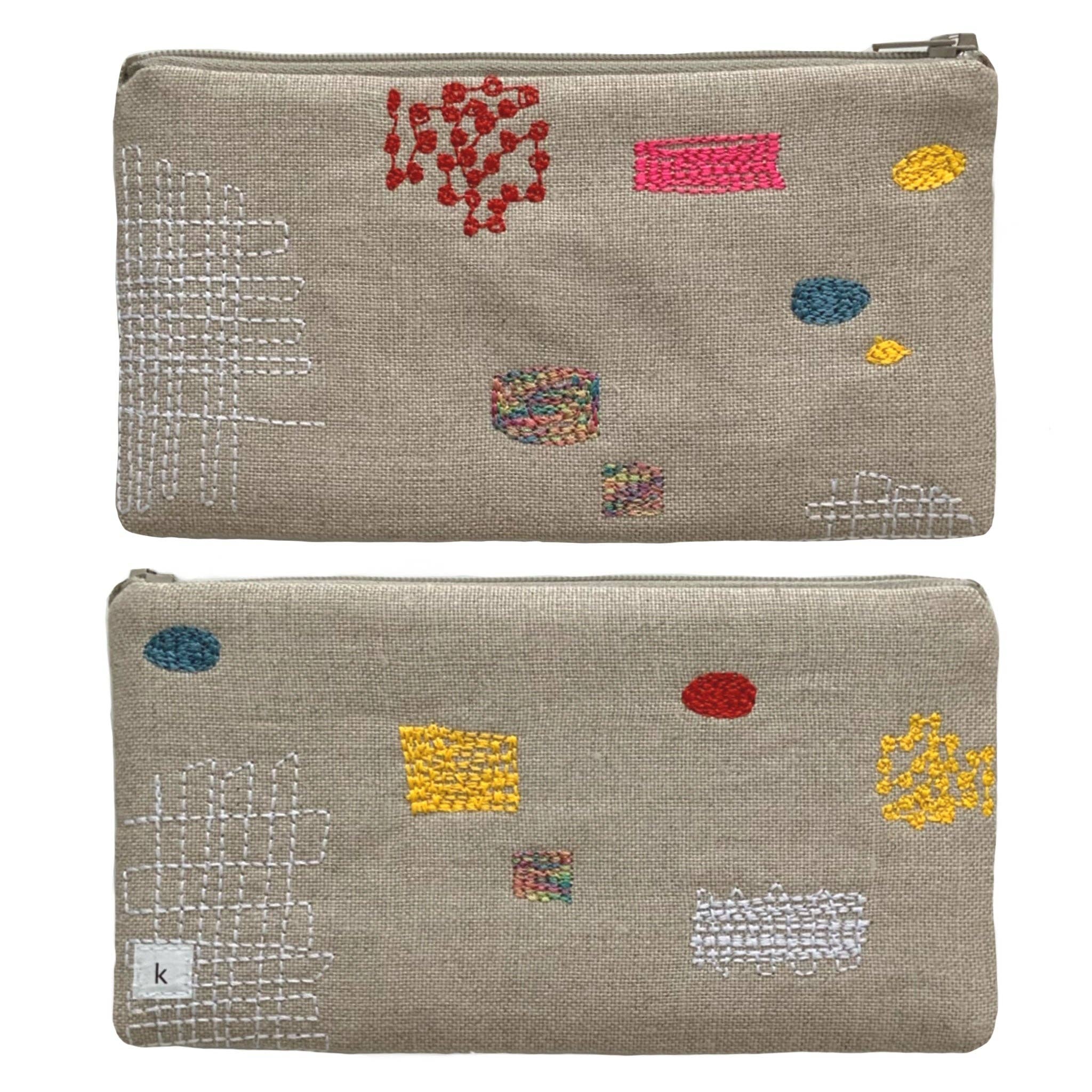 Patches Pouch by K Studio made of natural flax linen with colorful stitched patch motifs, slim rectangular shape, and zip closure on a neutral background.