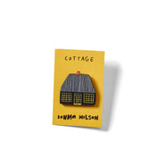Donna Wilson Cottage Pin featuring a black cottage with a striped roof and yellow windows, made from sustainably sourced beech wood with a metal butterfly clutch backing.