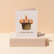 Red Cap Cards A Cake Card by Jon Klassen featuring an orange cupcake with eyes and a single birthday candle.