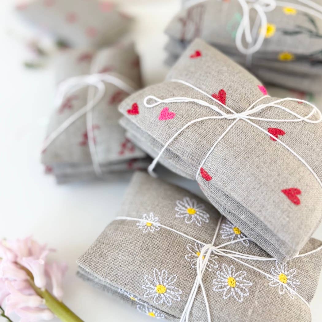 Micro Hearts Sachet Set by K Studio with three small flax linen sachets embroidered with tiny pink and red hearts, filled with lavender and arranged on a white background.