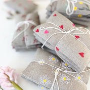 Micro Hearts Sachet Set by K Studio with three small flax linen sachets embroidered with tiny pink and red hearts, filled with lavender and arranged on a white background.