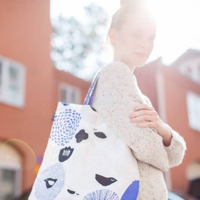 Person holding a blue floral and bird-pattern linen-cotton tote bag by Matti Pikkujämsä, 15" x 17".
