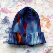 Painter's Hand-Dyed Beanie Hat by Merle Works in rich blue ribbed cotton-blend knit with hand-dyed splashes of purple, green, orange, and magenta, featuring a folded cuff and woven logo tag.