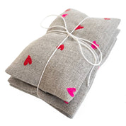 Micro Hearts Sachet Set by K Studio with three small flax linen sachets embroidered with tiny pink and red hearts, filled with lavender and arranged on a white background.