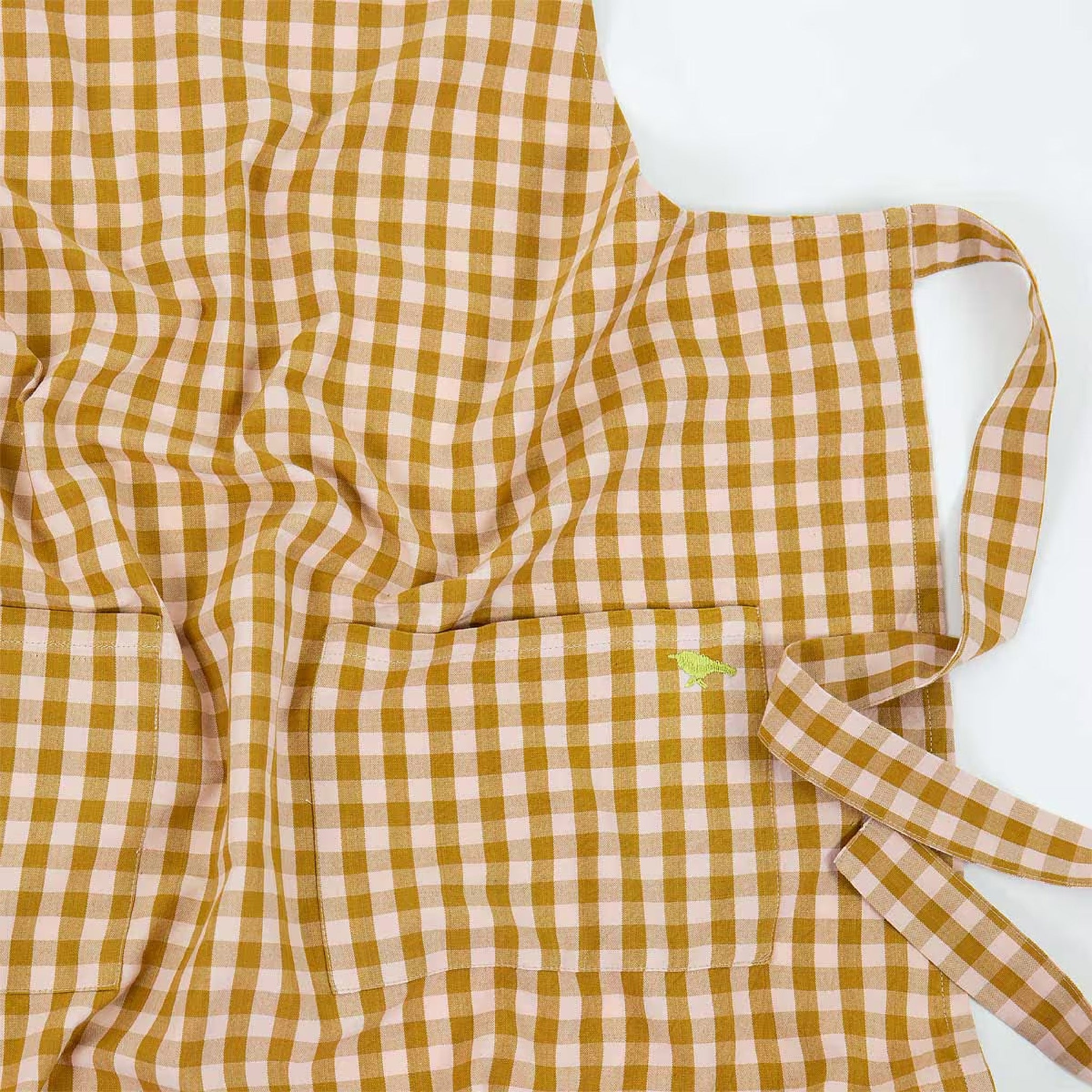 Maria Apron by A World of Craft in classic checkered organic cotton with two front pockets, adjustable neck strap, and signature embroidered yellow bird.