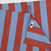 Nora Kitchen Towel by A World of Craft with wide blue and red handwoven cotton stripes, folded to show the bold striped pattern and textured reps weave.