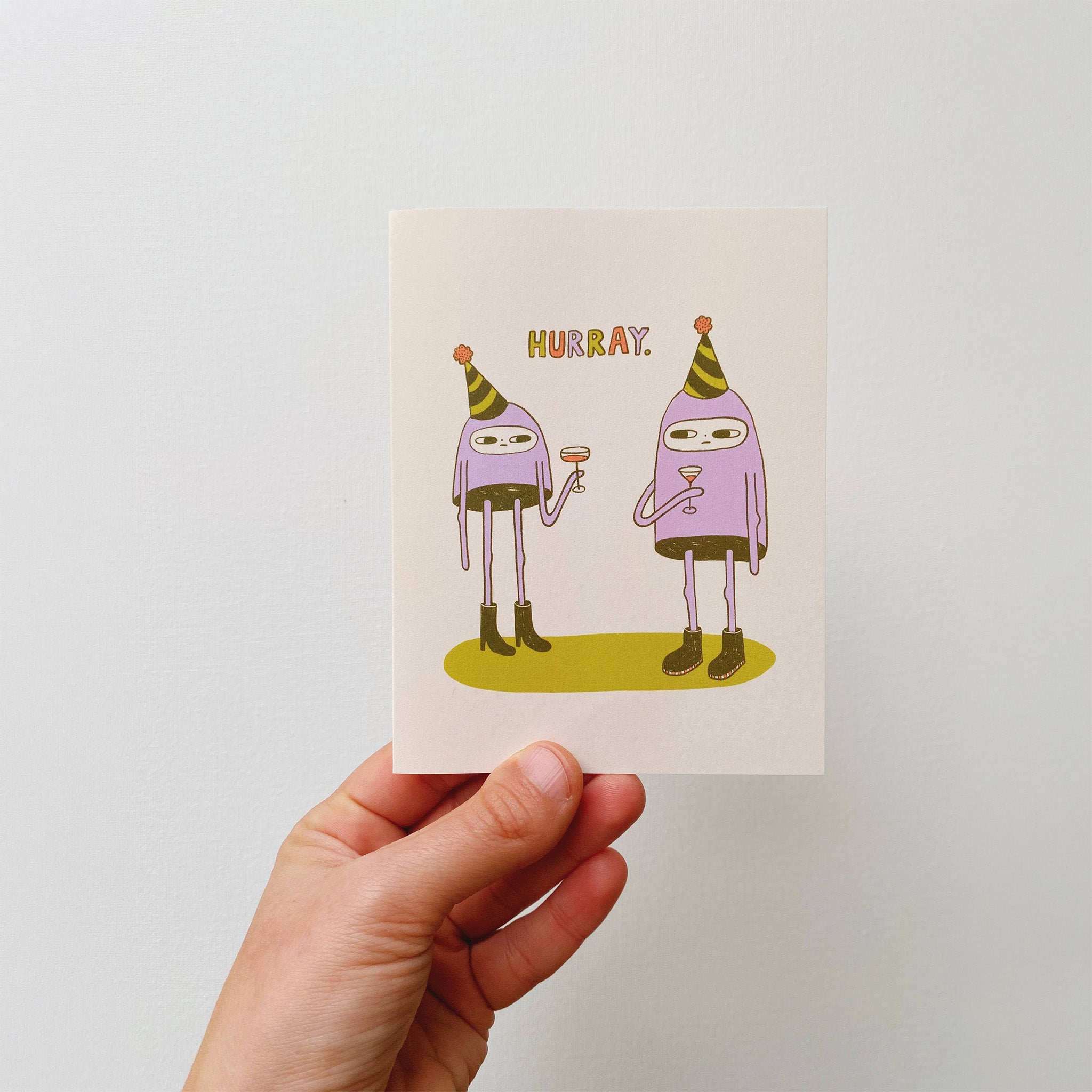 Hurray Card by Allison McKeen featuring two purple characters in striped party hats raising glasses beneath colorful “HURRAY” lettering.