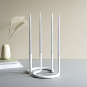 Architectmade Gemini Candleholder by Peter Karpf in matte white stainless steel, styled with matching white taper candles in a sculptural curved form.