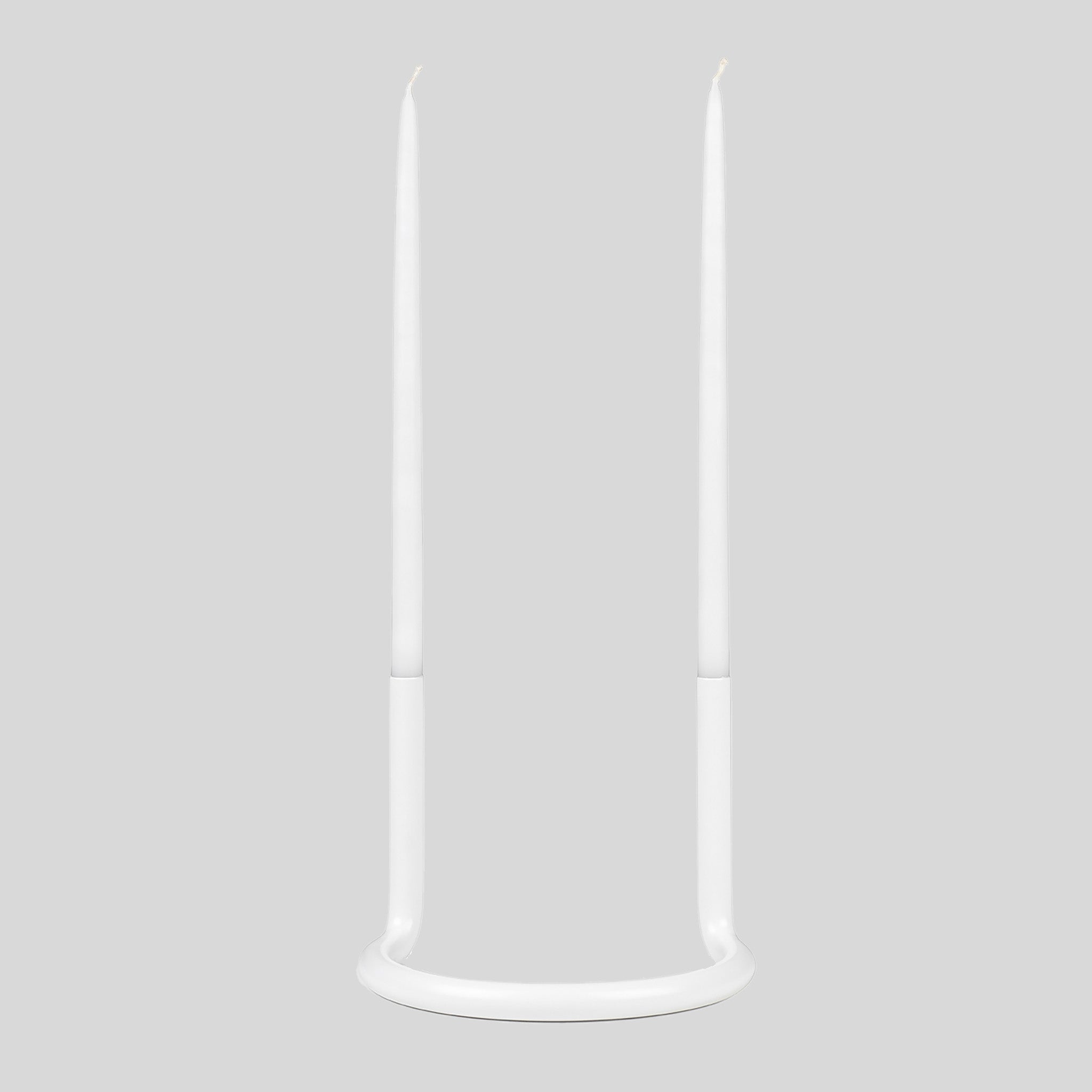 Architectmade Gemini Candleholder by Peter Karpf in matte white stainless steel, styled with matching white taper candles in a sculptural curved form.