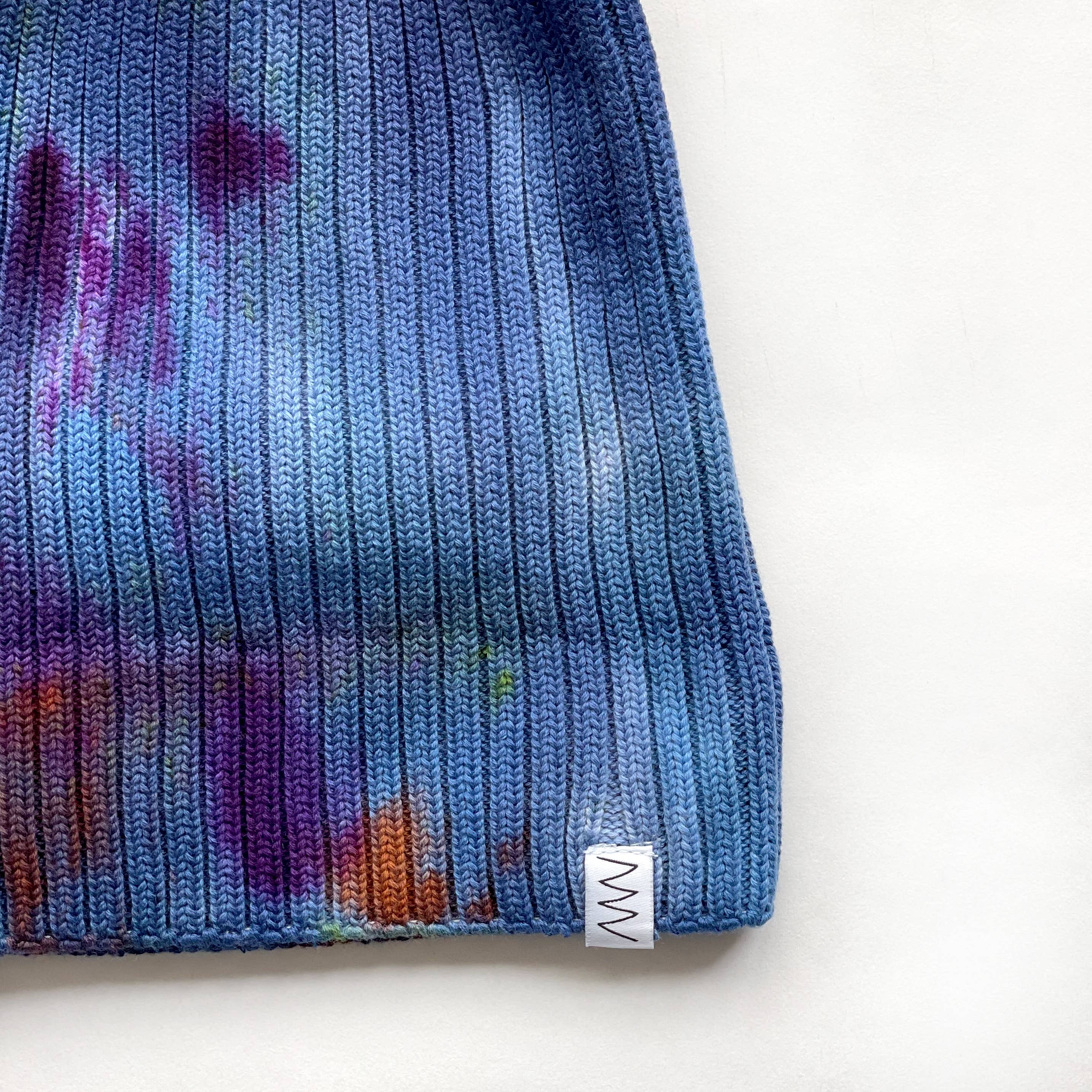 Painter's Hand-Dyed Beanie Hat by Merle Works in rich blue ribbed cotton-blend knit with hand-dyed splashes of purple, green, orange, and magenta, featuring a folded cuff and woven logo tag.