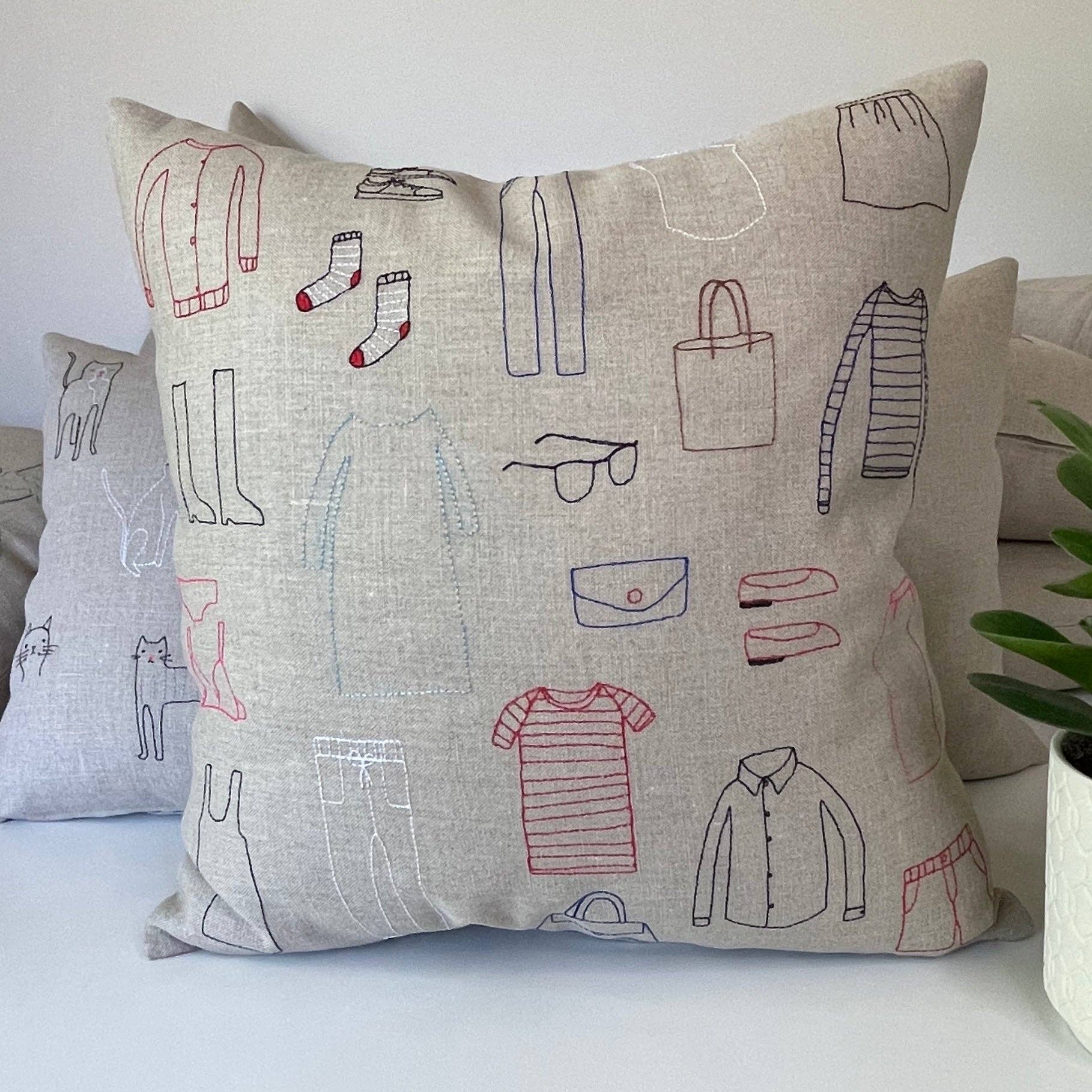 Clothes Cushion by K Studio. Handcrafted in Grand Rapids, Michigan. Flax linen pillow with multicolor stitched clothing motif, zipper closure, and down-alternative insert.