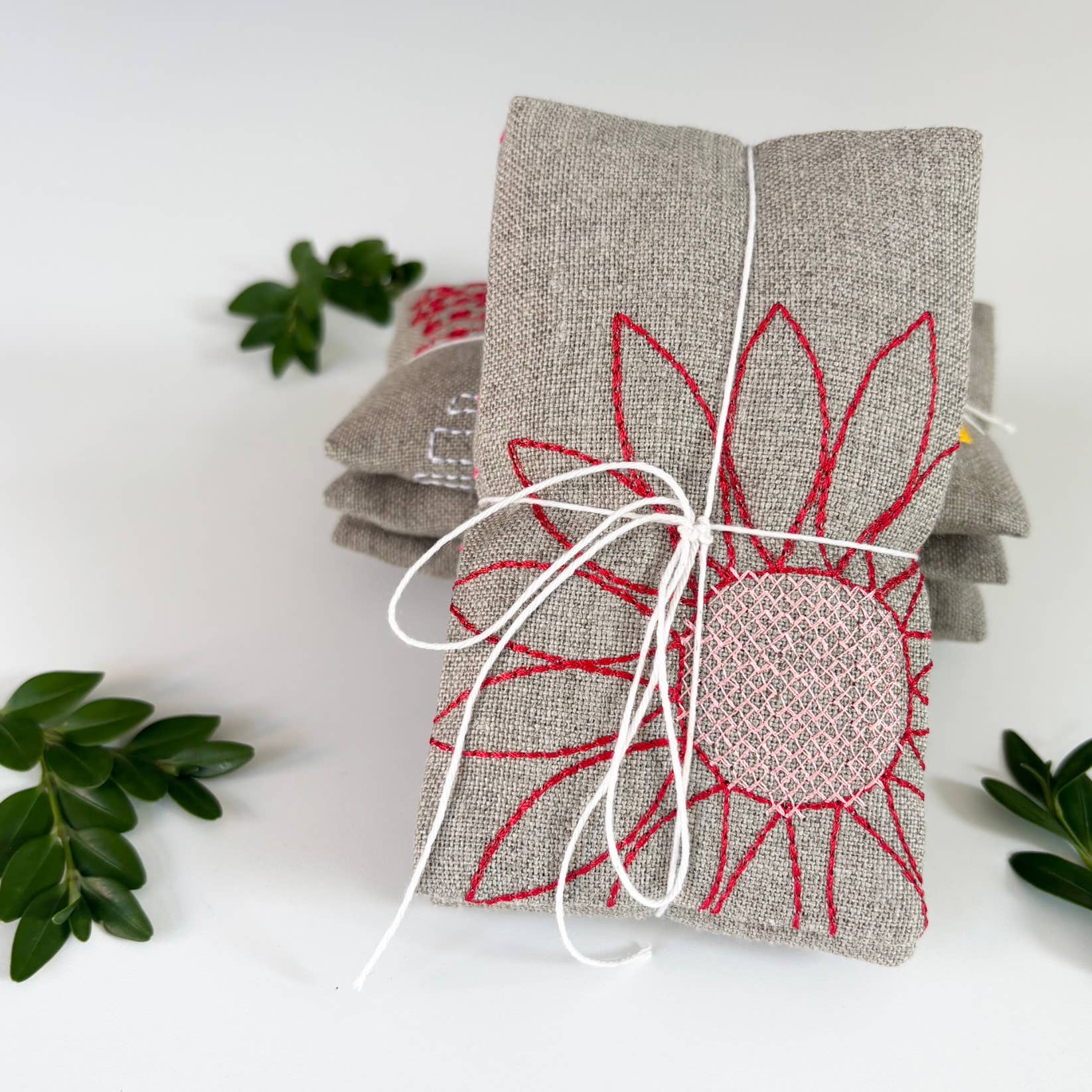 Blooms Sachet Set by K Studio with three flax linen sachets embroidered with colorful floral designs, filled with lavender and arranged on a white background.