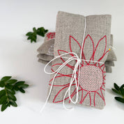 Blooms Sachet Set by K Studio with three flax linen sachets embroidered with colorful floral designs, filled with lavender and arranged on a white background.