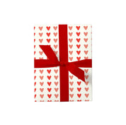 Hearts Gift Wrap with red and blush heart pattern on creamy white paper, wrapped around a gift and finished with a bold red ribbon.