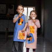 Spira of Sweden Daisy Kompisförkläde Kid’s Apron in pink cotton with hand-printed orange Daisy cat illustration, front pocket and adjustable neck strap.