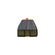Donna Wilson Cottage Pin featuring a black cottage with a striped roof and yellow windows, made from sustainably sourced beech wood with a metal butterfly clutch backing.