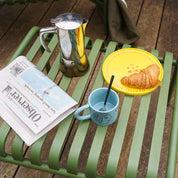 Teal-blue Donna Wilson stoneware mug with two debossed illustrated faces chatting on the side.
