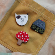 Donna Wilson Toadie Brooch Pin featuring a red and white spotted mushroom character with a friendly face, made from sustainably sourced beech wood with a metal butterfly clutch backing.
