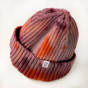 Brunette Hand-Dyed Beanie Hat by Merle Works featuring a ribbed cotton-blend knit in earthy shades of dusty rose, warm brown, rusty orange, and pink, with a folded cuff and woven logo tag.