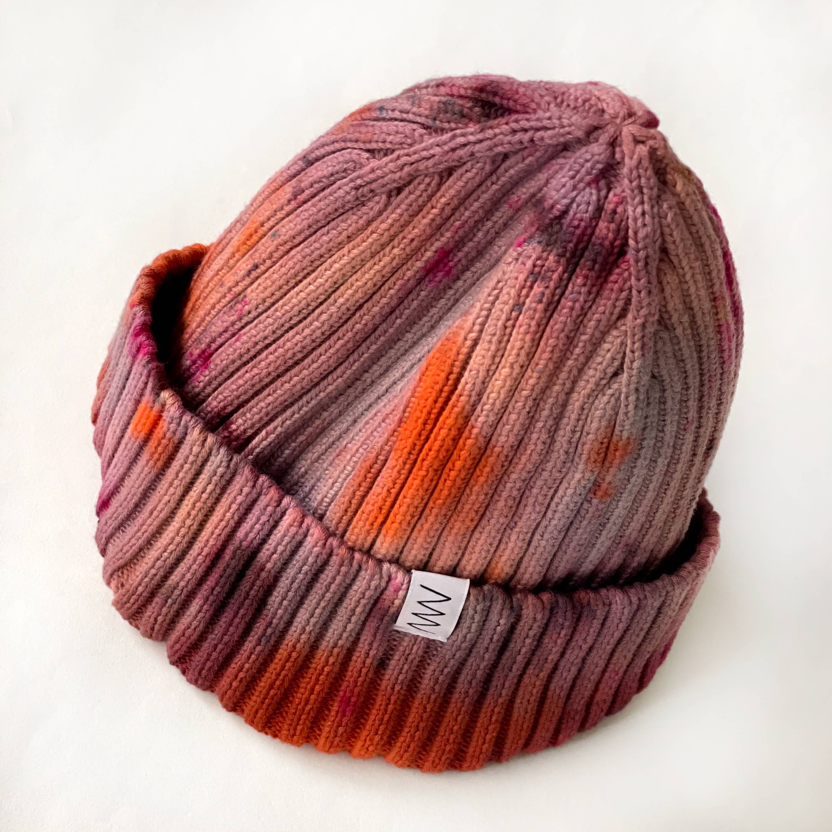 Brunette Hand-Dyed Beanie Hat by Merle Works featuring a ribbed cotton-blend knit in earthy shades of dusty rose, warm brown, rusty orange, and pink, with a folded cuff and woven logo tag.