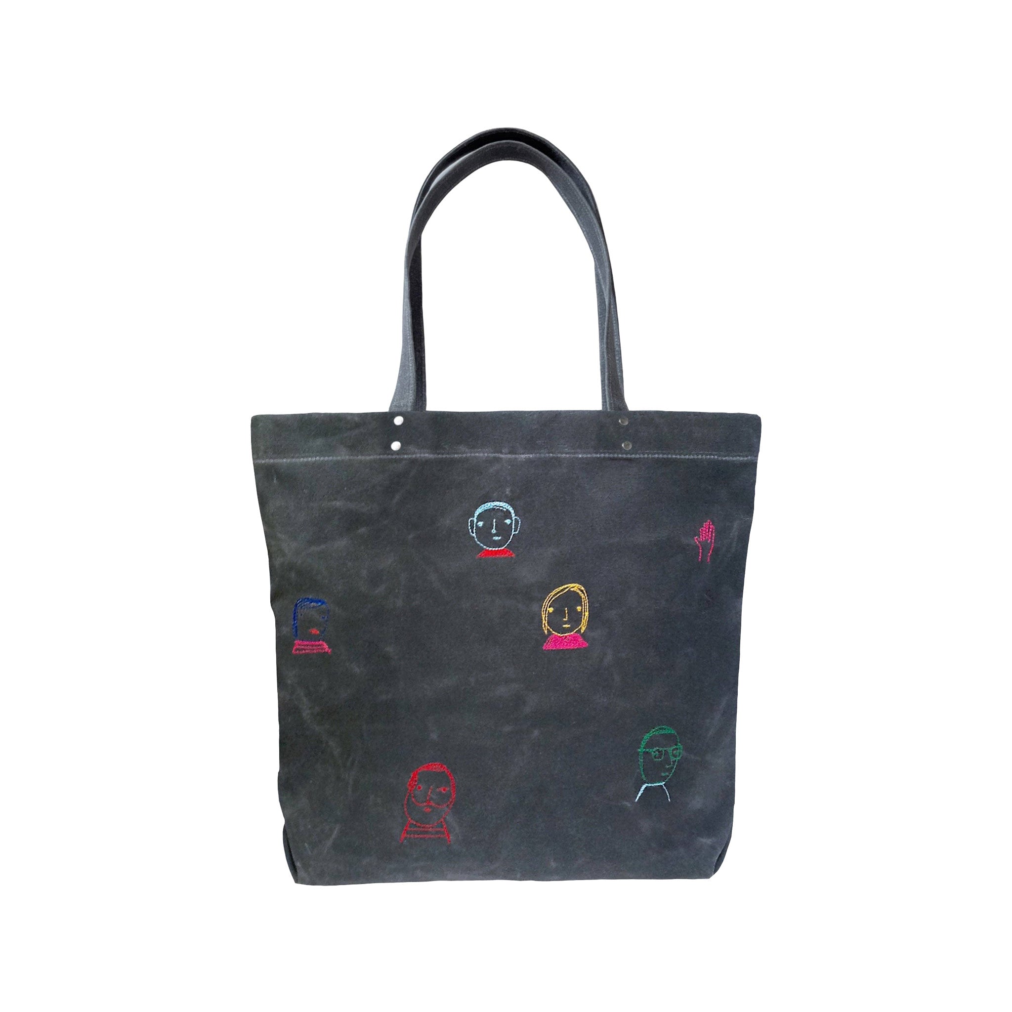 Folks Tote by K Studio in black waxed canvas with colorful embroidered face motifs, long shoulder straps, and a magnetic snap closure.