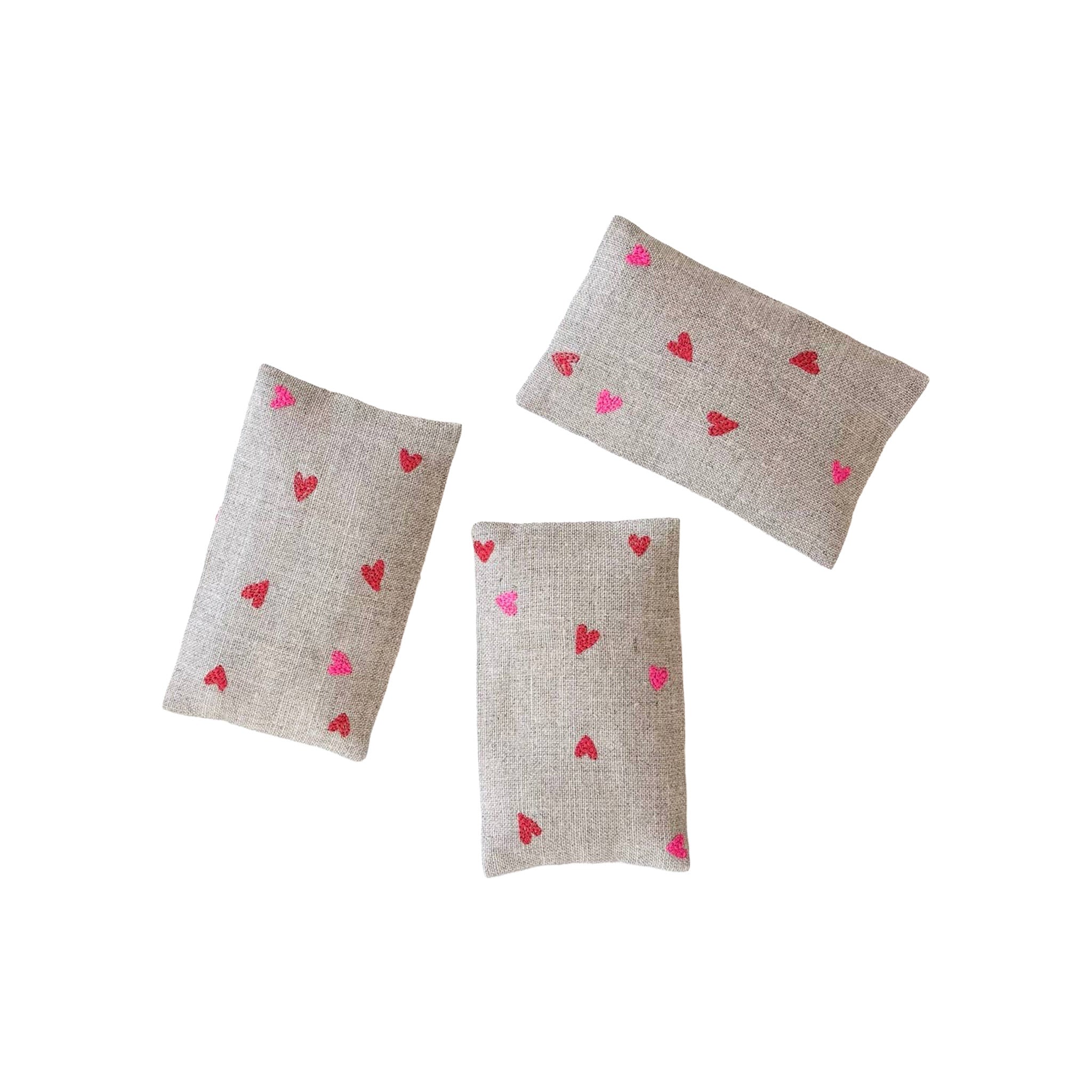 Micro Hearts Sachet Set by K Studio with three small flax linen sachets embroidered with tiny pink and red hearts, filled with lavender and arranged on a white background.