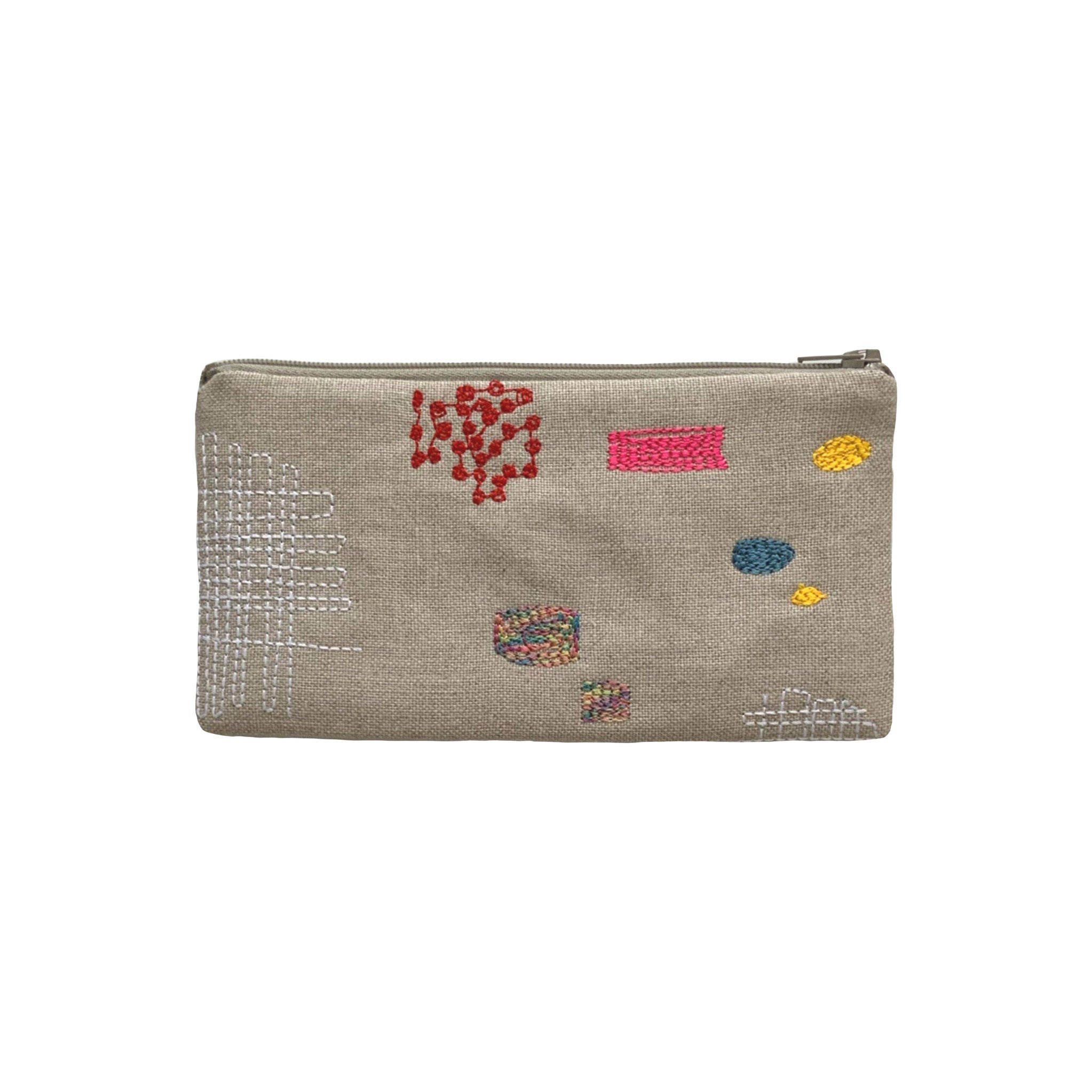 Patches Pouch by K Studio made of natural flax linen with colorful stitched patch motifs, slim rectangular shape, and zip closure on a neutral background.