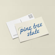 Little Something Co. Greetings from the Pine Tree State Postcard with retro blue lettering and small green text on a cream background.