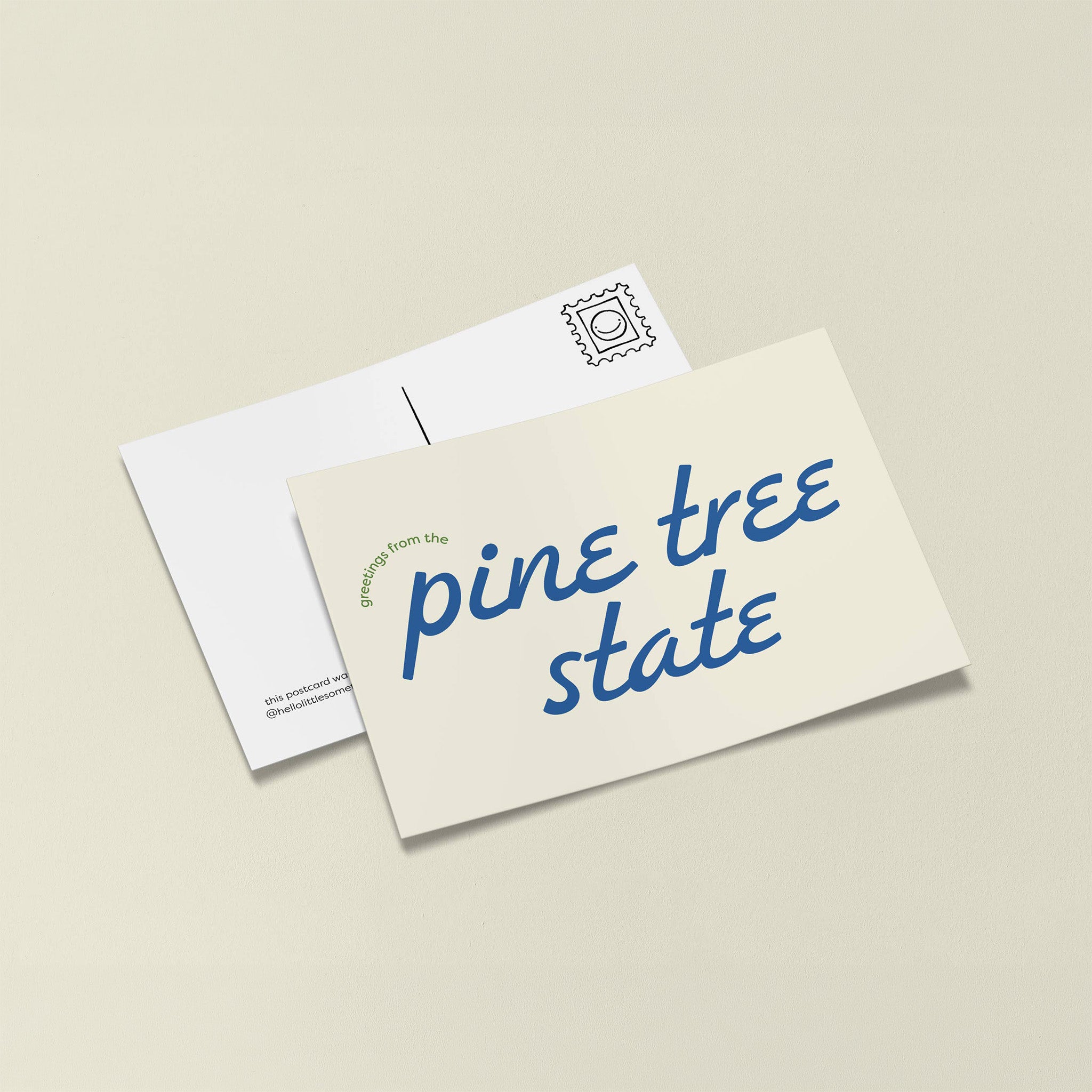 Little Something Co. Greetings from the Pine Tree State Postcard with retro blue lettering and small green text on a cream background.