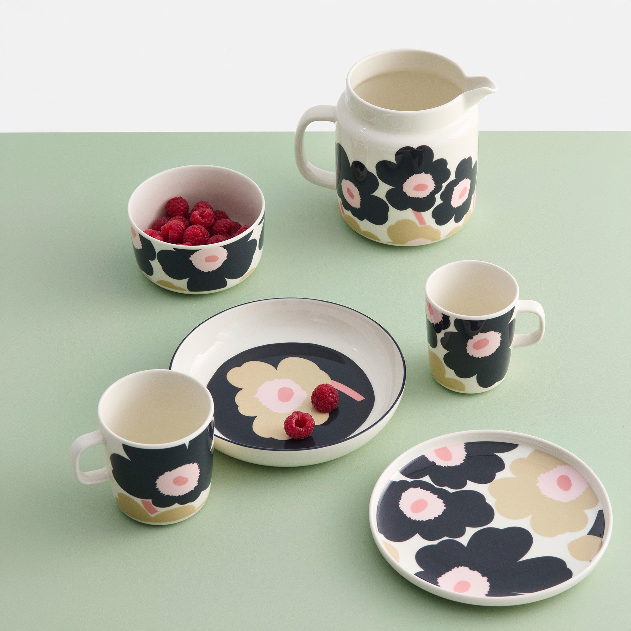 Oiva Unikko dinnerware collection by Marimekko in charcoal, sand, and pink floral pattern, including stoneware plate, mug, bowl, and pitcher in modern Scandinavian design.