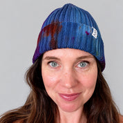 Painter's Hand-Dyed Beanie Hat by Merle Works in rich blue ribbed cotton-blend knit with hand-dyed splashes of purple, green, orange, and magenta, featuring a folded cuff and woven logo tag.