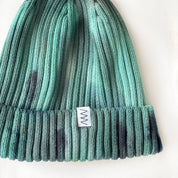 Evergreen Hand-Dyed Beanie Hat by Merle Works featuring a ribbed cotton-blend knit in varied shades of forest green, mint, and teal with darker hand-dyed speckles and a folded cuff.