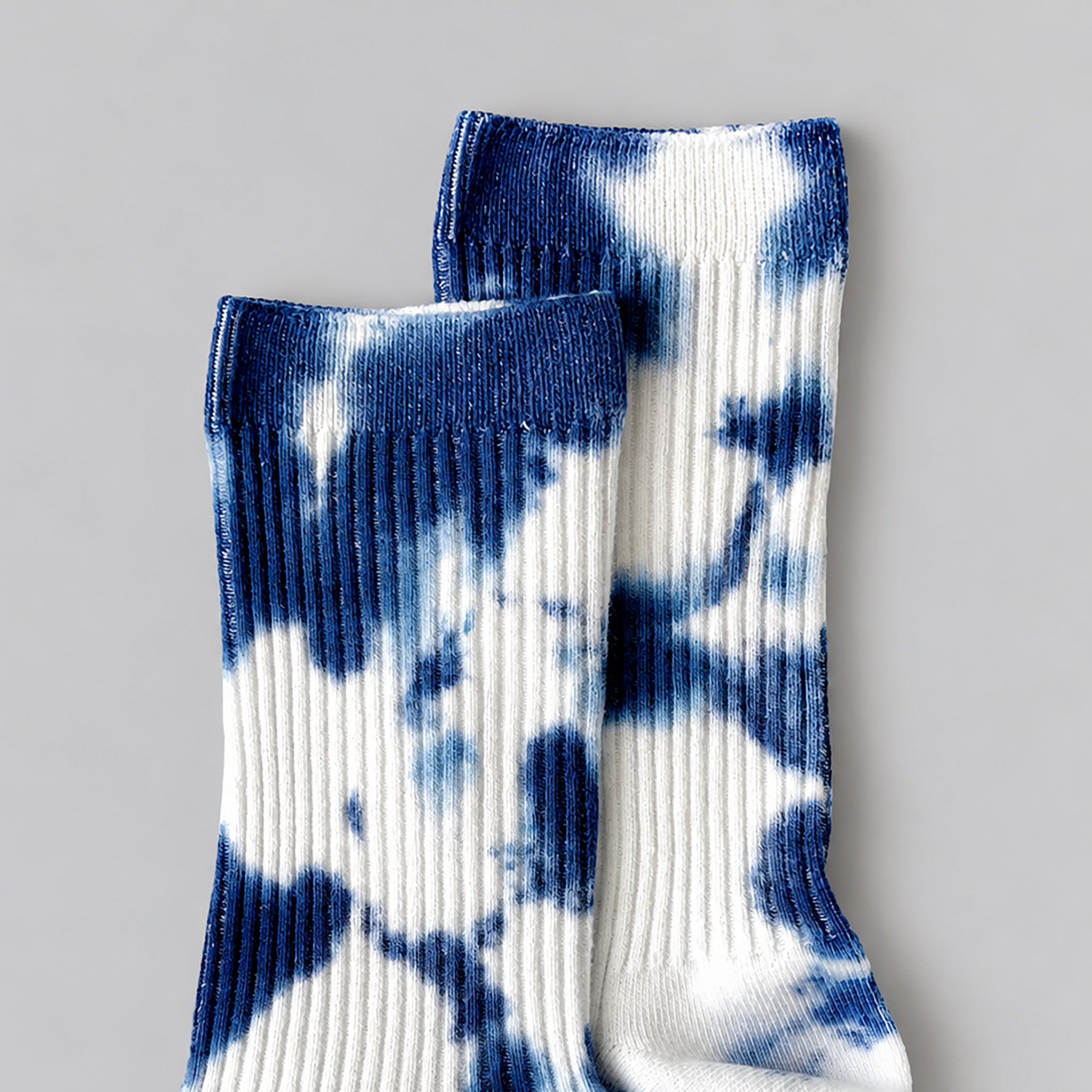 Indigo Tie-Dye Dressy Socks by Merle Works featuring white ribbed cotton with bold, irregular indigo blue hand-dyed patterns, arranged as an overlapping pair.