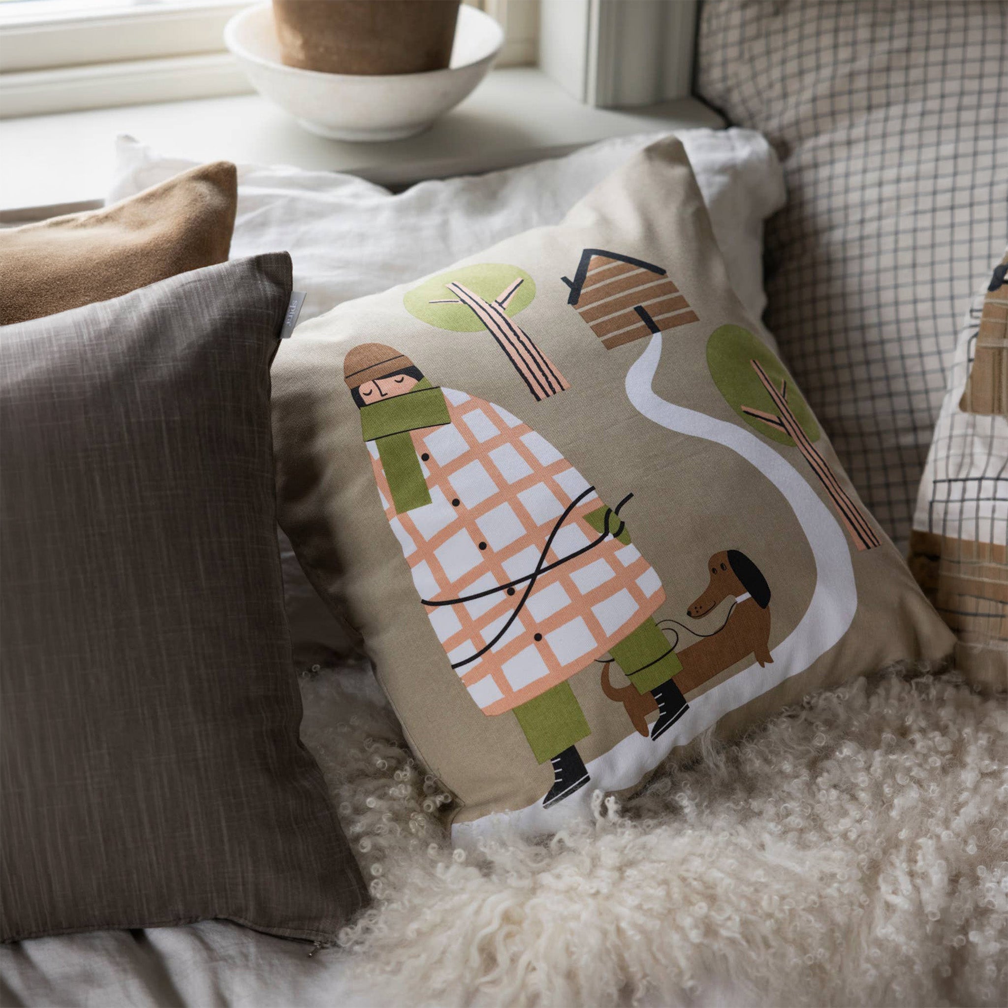 Hundpromenad Kompiskudde Cushion Cover by Spira of Sweden with hand-printed dog walker and dachshund illustration in warm autumn tones on beige cotton.
