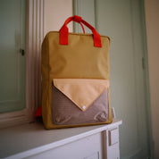 Sticky Lemon Envelope Backpack in colorful recycled fabric with front zip pocket, waterproof lining, and adjustable shoulder straps. Available in Small, Medium, and Large.