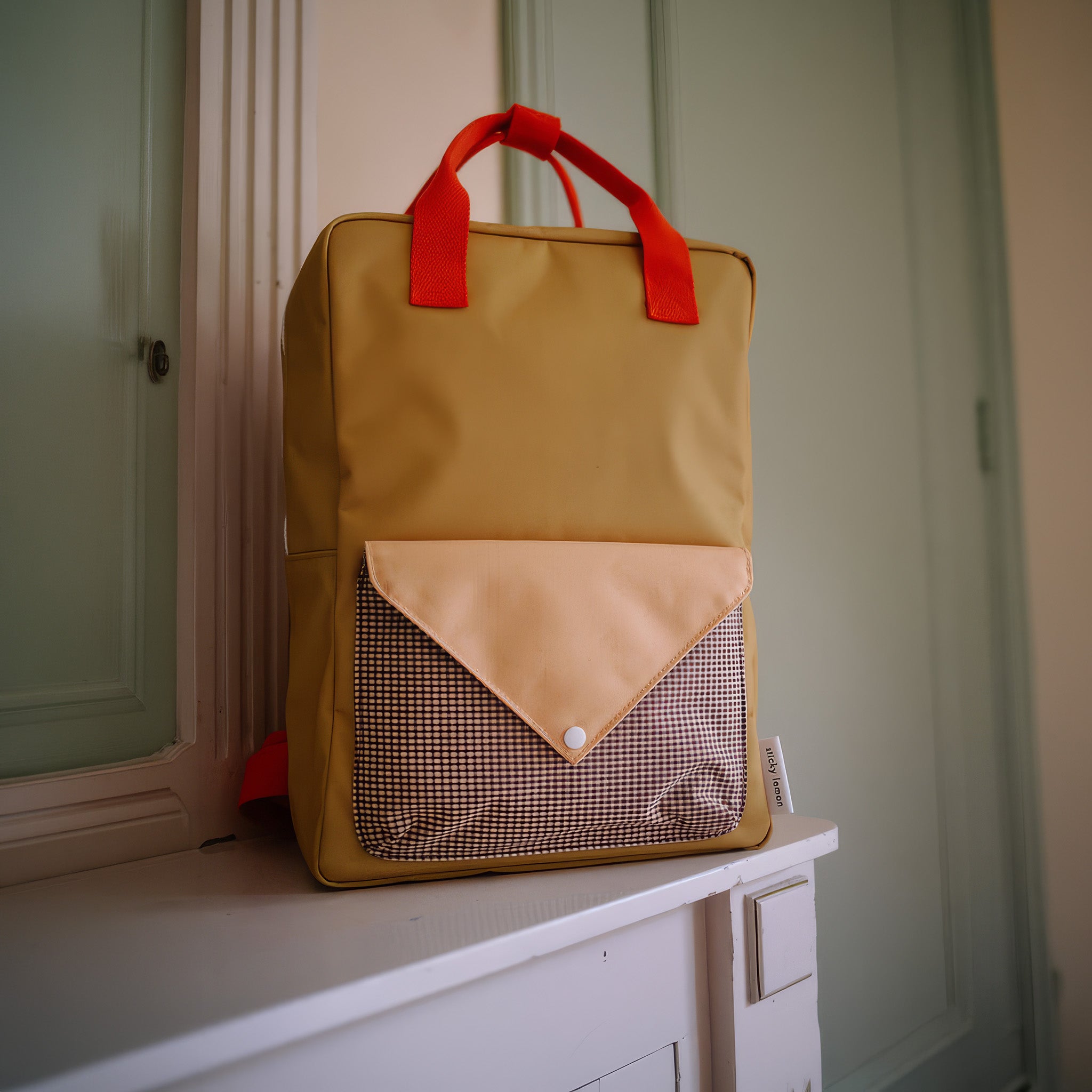 Sticky Lemon Envelope Backpack in colorful recycled fabric with front zip pocket, waterproof lining, and adjustable shoulder straps. Available in Small, Medium, and Large.