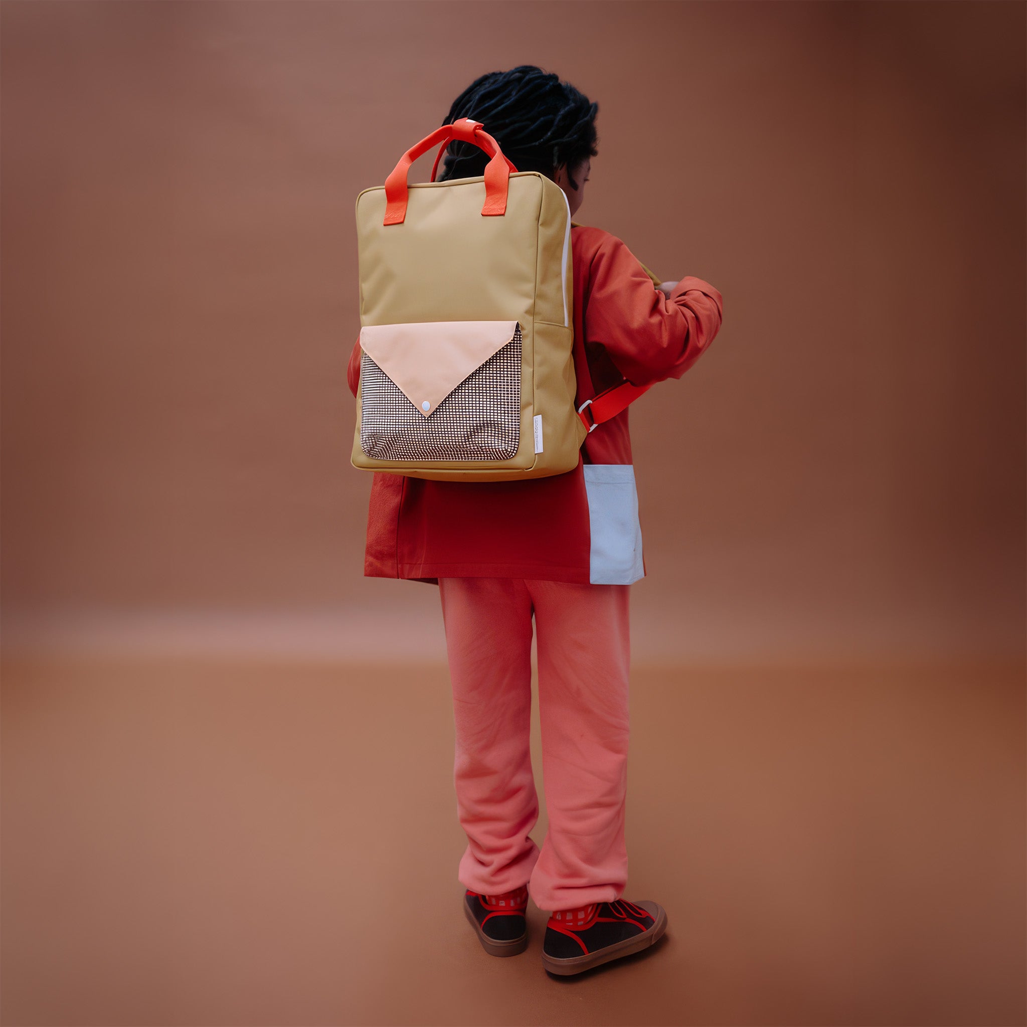 Sticky Lemon Envelope Backpack in colorful recycled fabric with front zip pocket, waterproof lining, and adjustable shoulder straps. Available in Small, Medium, and Large.