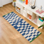 Blox Rug by Tarta Gelatina in Bleu, featuring an irregular blue and cream checkerboard pattern with bright green trim at both ends. Handmade from 100% cotton.