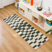 Blox Rug by Tarta Gelatina in Rosin, featuring an irregular forest green and cream checkerboard pattern with soft pink trim at both ends. Handmade from 100% cotton.