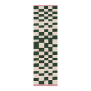 Blox Rug by Tarta Gelatina in Rosin, featuring an irregular forest green and cream checkerboard pattern with soft pink trim at both ends. Handmade from 100% cotton.