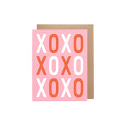 XOXO Valentine Card with bold hand-lettered XOXO pattern printed in dark ink on pink recycled cardstock, A2 folded, blank inside.